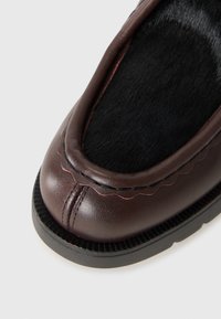 Scarpa in pelle marrone con superficie liscia, punta arrotondata e inserto in pelliccia nera. Presenta cuciture ondulate e una suola in gomma strutturata.