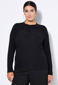Schwarzes Langarmshirt mit einem strukturierten Blumenmuster, rundem Ausschnitt und lässigem Schnitt, kombiniert mit schwarzen Hosen.