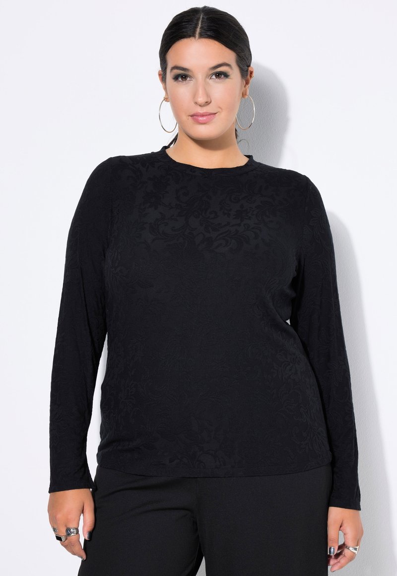 Schwarzes Langarmshirt mit einem strukturierten Blumenmuster, rundem Ausschnitt und lässigem Schnitt, kombiniert mit schwarzen Hosen.