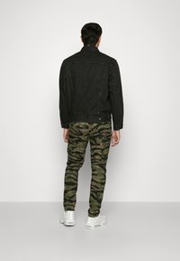 Jachetă din denim neagră cu un croi lejer, asortată cu pantaloni verzi cu camuflaj, având un model cu frunze. Adidașii albi completează ținuta.