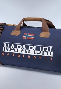 Tummansininen reppu, joka on valmistettu kestävästä kankaasta. Ominaisuuksiin kuuluvat ruskeat yksityiskohdat, tukevat kahvat ja läppä, jossa on Norjan lippu. Suuri logo-teksti.
