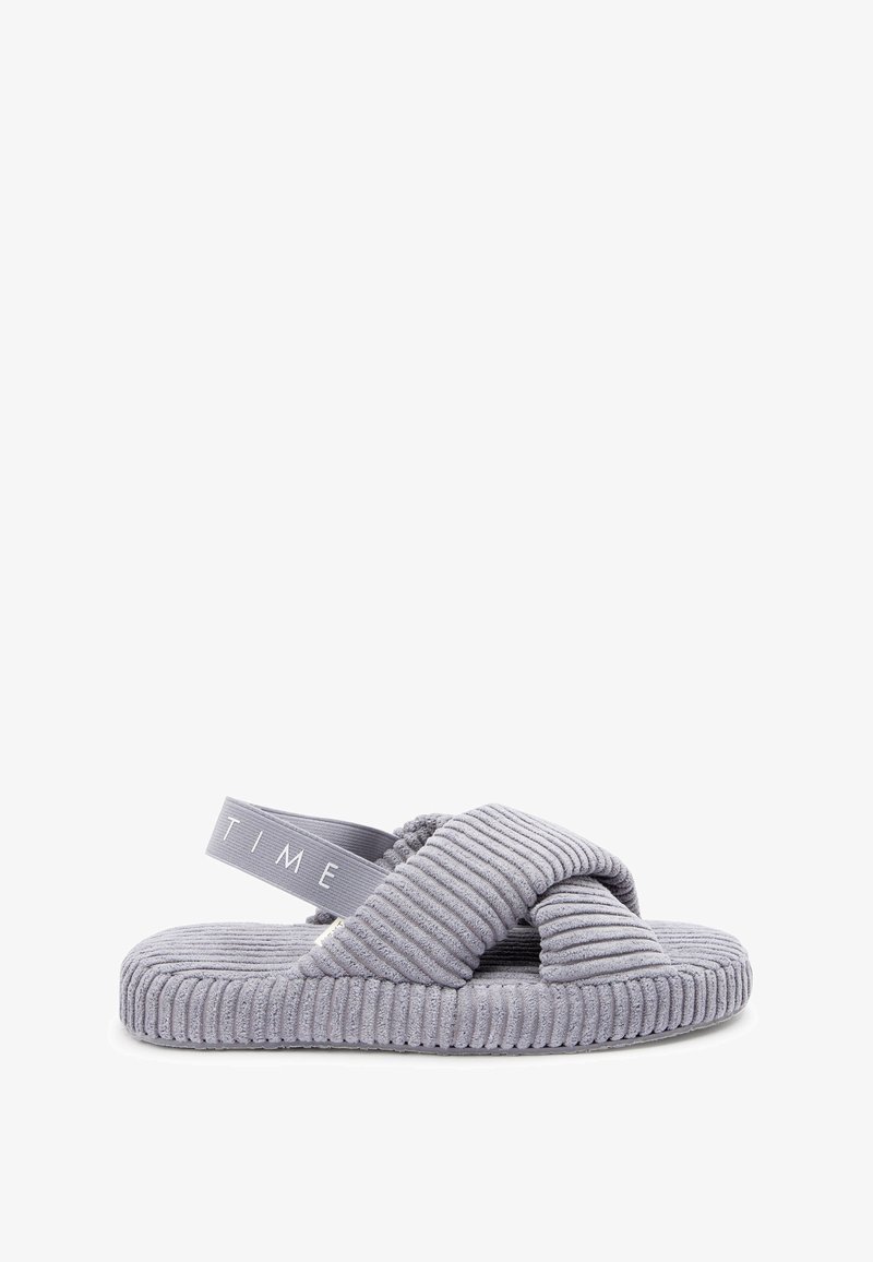 Mocassin gris avec texture nervurée, design croisé et semelle plate. Comprend une tige en tissu doux et une sangle de cheville élastique avec logo.