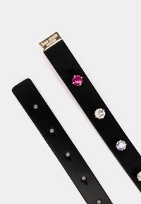 Schwarzes Lederarmband mit fünf farbigen Steinen: einem rosa, einem klaren und einem lila, die in goldfarbenen Krallen eingesetzt sind. Beinhaltet eine goldene Logo-Plakette.