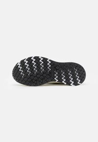 Semelle de chaussure en caoutchouc noir avec un motif zigzag blanc et une texture de grip multidirectionnelle. Semelle conçue pour offrir une adhérence sur diverses surfaces.