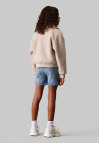 Giacca beige fluffy dallo stile relaxed, abbinata a short in denim blu chiaro. Sneakers bianche e polsini a coste completano l'outfit.