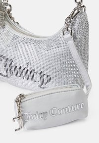 Ezüst strasszkövekkel díszített, ívelt formájú kézitáska, amelyhez egy leválasztható, ezüst selyem kis tasak tartozik, rajta a "Juicy Couture" felirattal.
