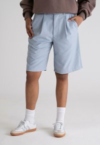 Light blue pleated shorts with side pockets, made from a smooth fabric, paired with white sneakers and ribbed white socks.
