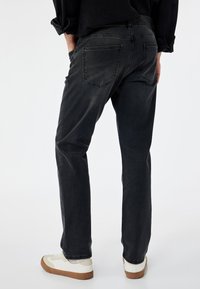 Jeans de mezclilla gris oscuro con un diseño de pierna recta, cinco bolsillos, un sutil desgaste y costuras en la parte superior. Combinados con zapatillas blancas y marrones.