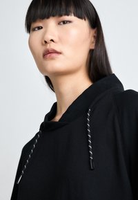 Black hoodie with a drawstring hood, featuring contrasting black and white cords and a soft texture. Simple, minimalist design details.