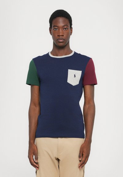 T-shirt à manches courtes en tissu mélangé de coton, avec un corps bleu marine, des manches vertes et bordeaux, une poche grise et un logo brodé.