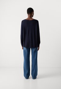 Marineblå langermet topp med løs passform og rund hals, kombinert med lyseblå vide jeans, sett bakfra.