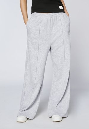 Person wearing loose light gray sweatpants with front seams and white sneakers, hands in pockets, against plain background.