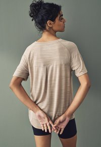 Top de manga corta beige con un ajuste ligeramente holgado, que presenta una costura horizontal y una textura sutil. Pantalones cortos deportivos negros visibles por debajo.