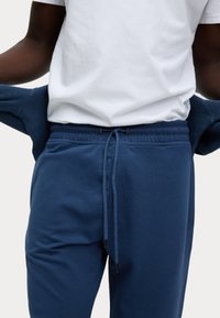 Blauwe katoenen sportbroek met een elastische tailleband, trekkoordsluiting en zijzakken. Gepaard met een witte T-shirt met ronde hals.