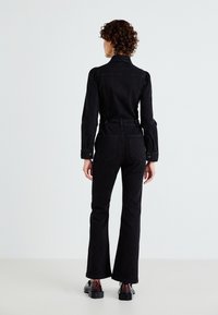 Črn denim overall s prilegajočo silhueto, dolgimi rokavi in širokimi hlačnicami. Ima sprednje žepe in pas, obdan z pasom. Teksturovan material.
