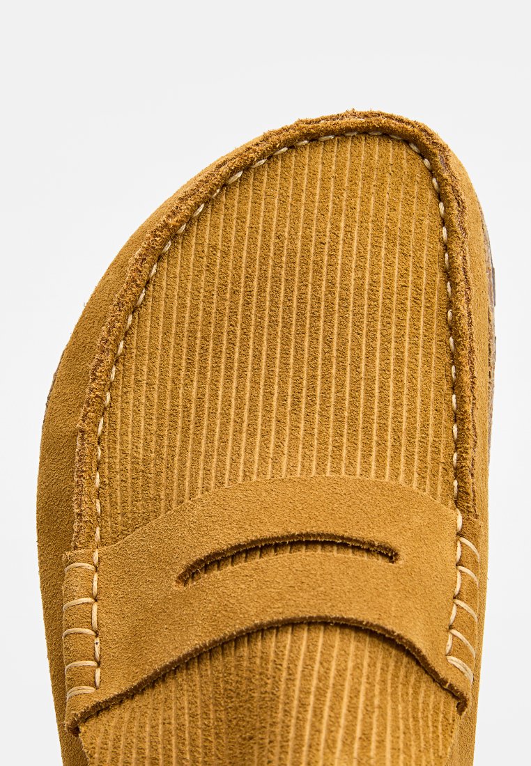 Gros plan sur le mocassin en cuir suédé marron avec des coutures détaillées et une texture striée sur la zone des orteils.