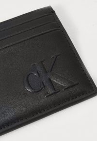Portafoglio in pelle nera con logo "CK" in rilievo, numerosi scomparti per carte e bordi finemente cuciti; la superficie ha una finitura testurizzata.