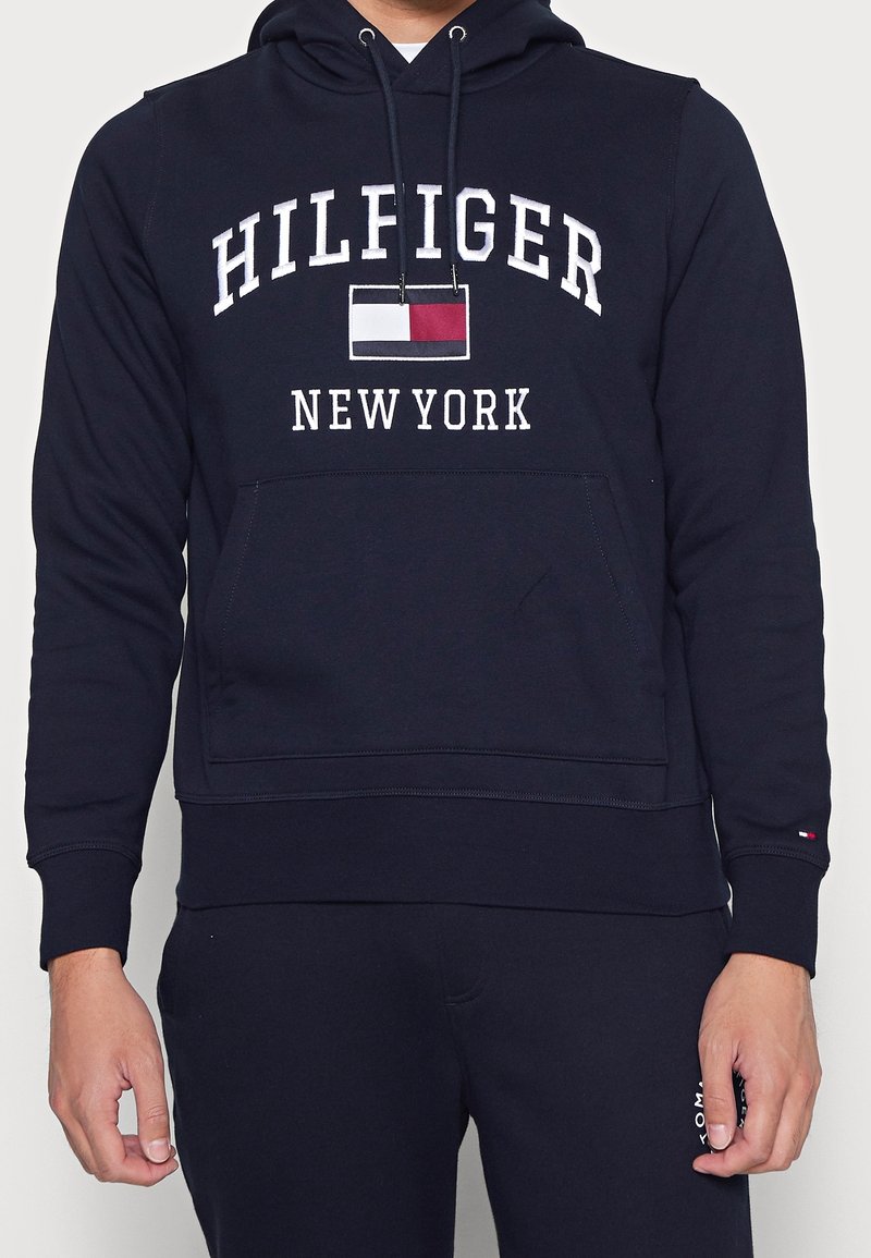 Sudadera navy con bolsillo frontal, con el texto "HILFIGER" y "NEW YORK" en blanco, además de un pequeño logo de bandera. Fabricada con tejido texturizado.