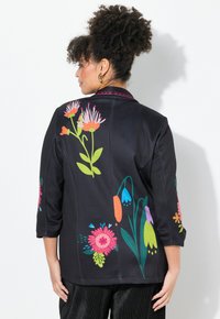 Schwarze Jacke mit buntem Blumenstickerei auf dem Rücken und den Ärmeln; Dreiviertelärmel und ein kontrastierender gemusterter Kragen.