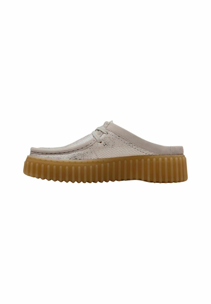 Beige slip-on shoes with a textured upper, light sheen, and a thick, ridged gum sole. Minimal lacing detail and rounded toe design.