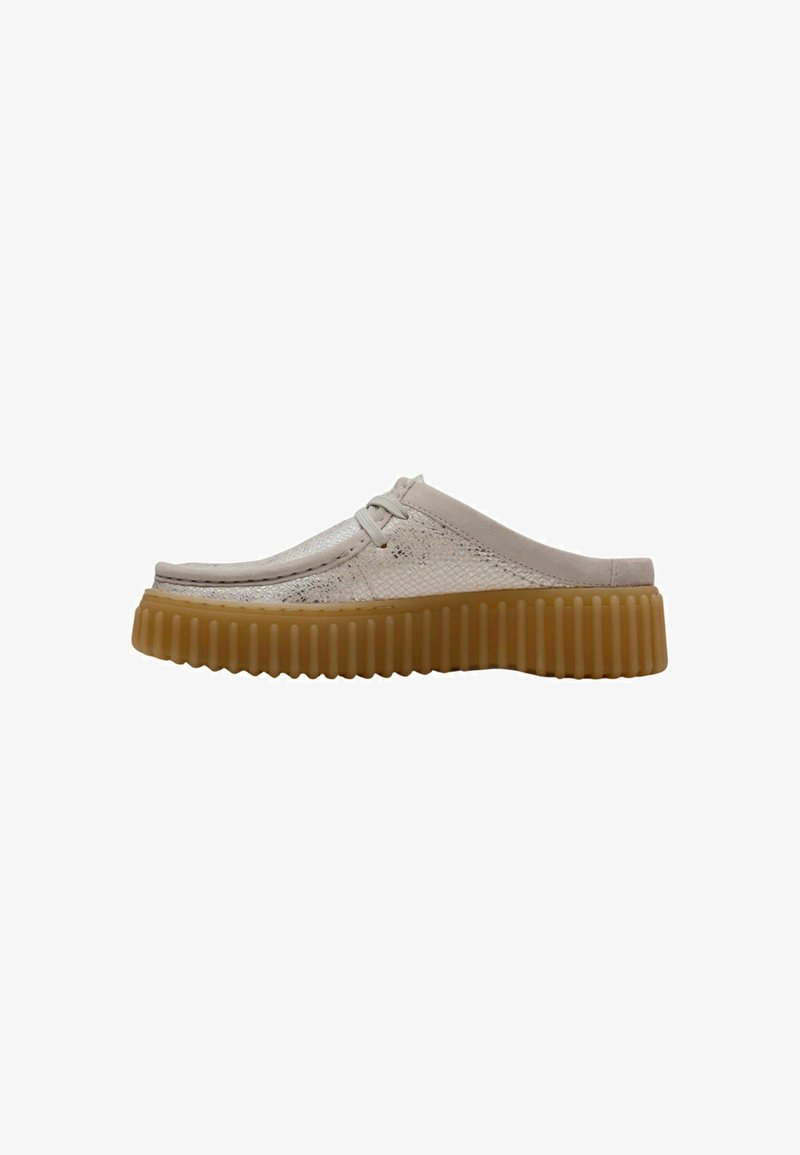 Scarpe beige slip-on con una tomaia testurizzata, leggera lucentezza e una suola in gomma spessa e scanalata. Dettagli di allacciatura minimale e design della punta arrotondata.
