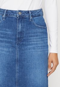 Jeanskjol i medelblått med rak skärning, hög midja, framfickor och en synlig söm fram. Slät textur och minimala sömnadsdetaljer.