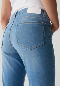 Jean en denim bleu clair avec un design classique à cinq poches, une couture de dos et une étiquette de marque blanche à la taille.