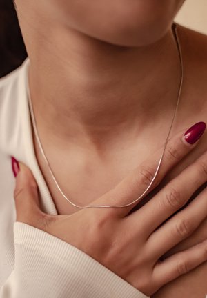 Silver necklace with a sleek, thin design resting on the neck, accompanied by a hand lightly touching the collarbone.