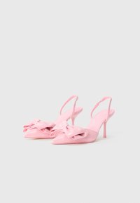 Vaaleanpunaiset patentoidut slingback-korkokengät, joissa on teräväkärkinen muotoilu ja ylisuuri nauhalausunto edessä, sekä kapea stiletto-korko.