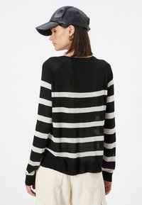 Sort og hvid stribet sweater med afslappet pasform, lange ærmer og rund halsudskæring. Letvægtstrikket stof og ribbet kant.