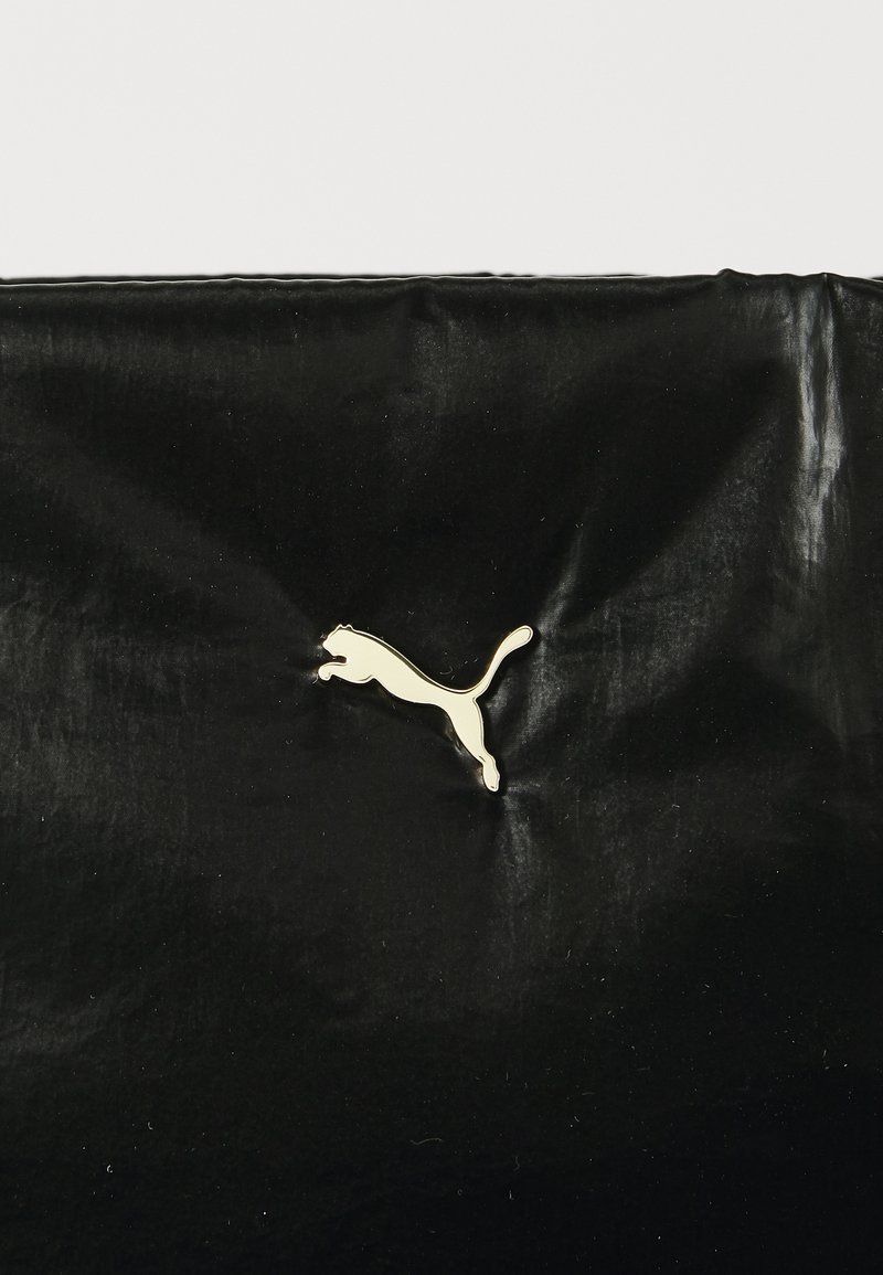 Bolsa negra con una superficie brillante y texturizada que presenta un logo dorado de puma saltando en el lateral. Material suave y diseño minimalista.