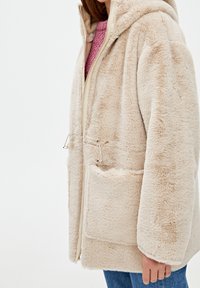 Beige faux fur hættejakke med frontlynlås, snor i taljen og frontlommer. Blød tekstur og afslappet pasform.