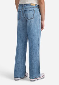 Jeans in denim blu a gamba larga con una texture sbiadita e cuciture arancioni. Include tasche posteriori e un'etichetta in pelle marrone sulla cintura.