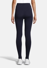 Marineblauwe high-waisted legging met een zachte textuur. Strak ontwerp, volledige lengte van de pijpen en een klein achterzakje, gecombineerd met witte sneakers.