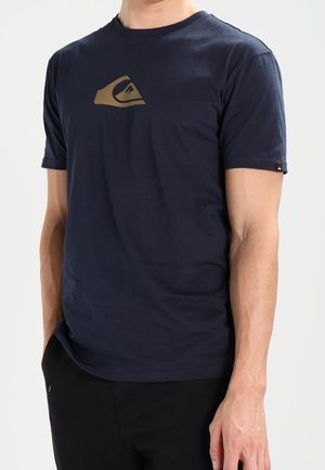 Mørkeblå t-shirt lavet af blød bomuld, med en stor lysebrun logo på brystet. Pasformen er afslappet med korte ærmer og rund hals.