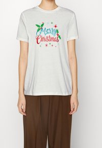 Bílá bavlněná trička s designem "Veselé Vánoce" v modré, červené a zelené barvě, zdobené větvičkami jmelí a hvězdičkami. Krátké rukávy a kulatý výstřih.