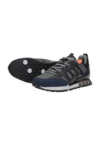 Zwarte en marineblauwe sport sneakers met grijze veters, honingraatpatroon op de zool en een oranje label op de hielkraag, gepositioneerd met één schoen rechtop en één zool omhoog.