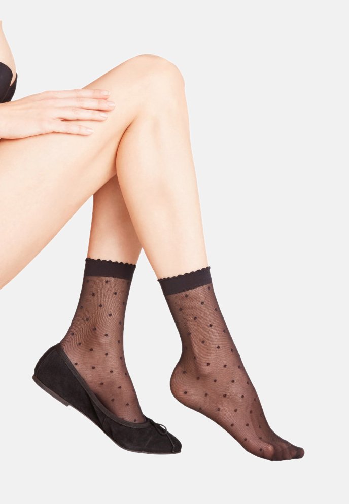 Schwarze Socken mit Polka-Dots und gewelltem Rand, aus durchsichtigem Material, die mit schwarzen Wildleder-Balletschuhen kombiniert sind.