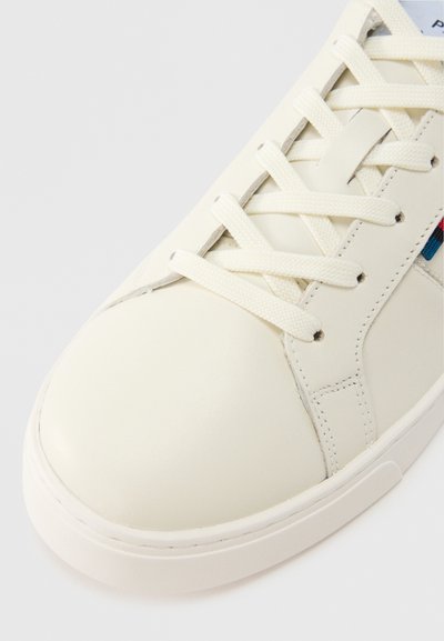 Biely kožený teniska s textúrovanými šnúrkami, zaoblenou špičkou, jemnými detailmi šitia a farebnými akcentmi na bočnom paneli.