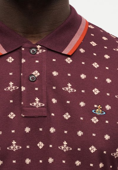 Κοντινό πλάνο μαρονού πόλο μπλουζάκι με ανοιχτομπεζ διαμαντένια σχέδια, δύο μαύρα κουμπιά και πολύχρωμο κεντητό λογότυπο σφαίρας στο στήθος.