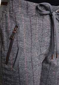 Szare dresowe spodnie z teksturowanej tkaniny, z pionowymi różowymi paskami, regulowanym sznurkiem w pasie oraz zamykanymi na zamek bocznymi kieszeniami.