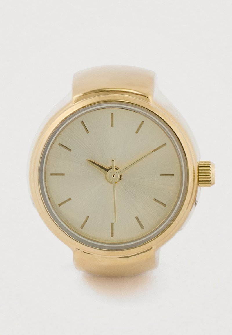 Αναλογικό ρολόι σε χρυσή απόχρωση με στρογγυλή θήκη, μινιμαλιστικό καντράν και ευθείες ενδείξεις ωρών. Λείο, γυαλιστερό φινίρισμα και υφασμένο επιφάνεια καντράν.