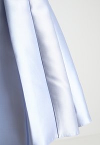 Pověšená jemně modrá hladká saténová látka s měkkými záhyby na jednobarevném světlém pozadí.