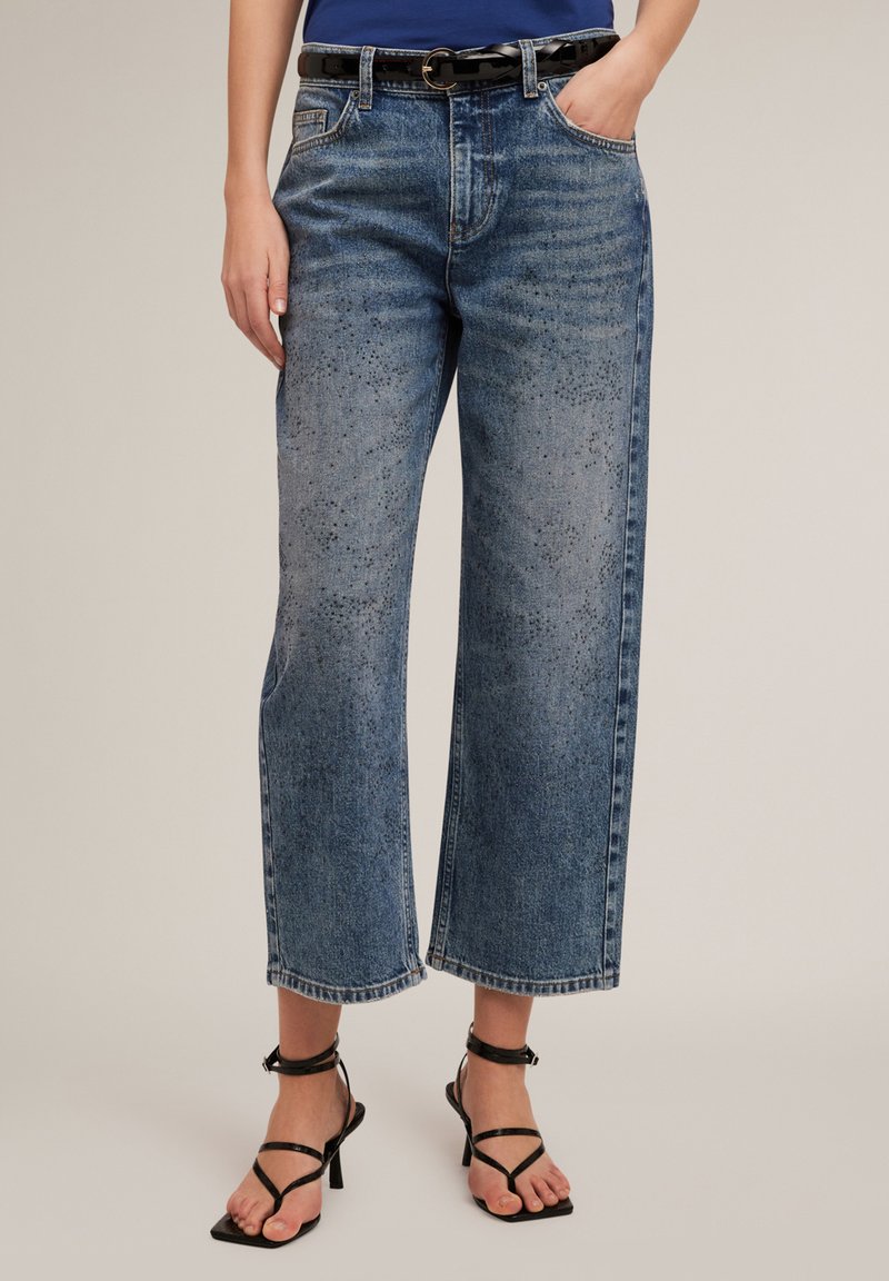 Jeans de mezclilla azul de pierna ancha con un lavado descolorido, con una cintura alta, bolsillos laterales y un cinturón negro con una hebilla redonda.