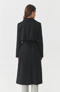 Black trench coat with a belted waist, long sleeves, back pleat detail, and a collar. Smooth texture, mid-length design.