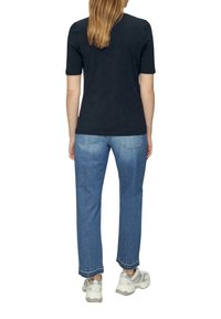 Haut noir à manches courtes associé à un jean droit bleu clair. Le modèle porte des baskets multicolores, montrant une tenue décontractée de dos.