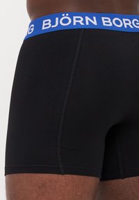 Schwarze Baumwoll-Boxershorts mit einem blauen Bund, der den weißen Text "BJÖRN BORG" trägt; glatte Textur, figurnaher Schnitt und subtile Nähdetails.
