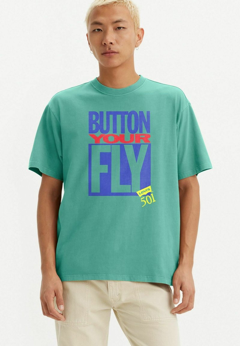 Turquoise cotton t-shirt featuring a graphic design with the text "BUTTON YOUR FLY" in red, blue, and yellow. Short sleeves and crew neck.