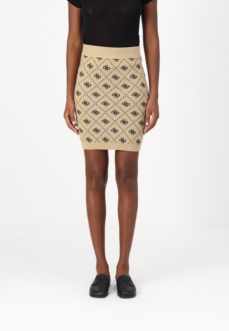Femme portant une jupe tricotée beige à motifs, un haut noir à manches courtes et des chaussures noires sans lacets, debout sur un fond blanc.