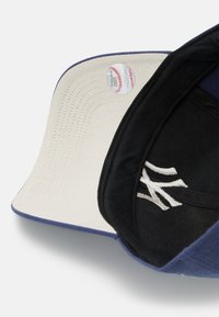 Marineblaue Baseballmütze mit einem schwarzen Innenfutter, einem weißen gestickten Logo und einer cremefarbenen Unterseite des Schirms mit sichtbaren Nähten und einem Etikett.